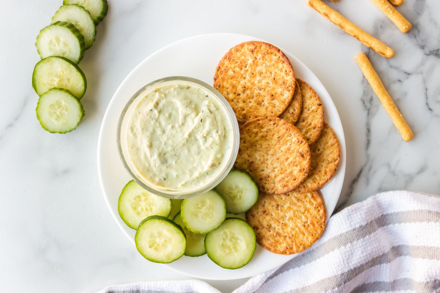 Avocado ranch dip with Greek yogurt served in a small bowl with sliced cucumbers and crackers.