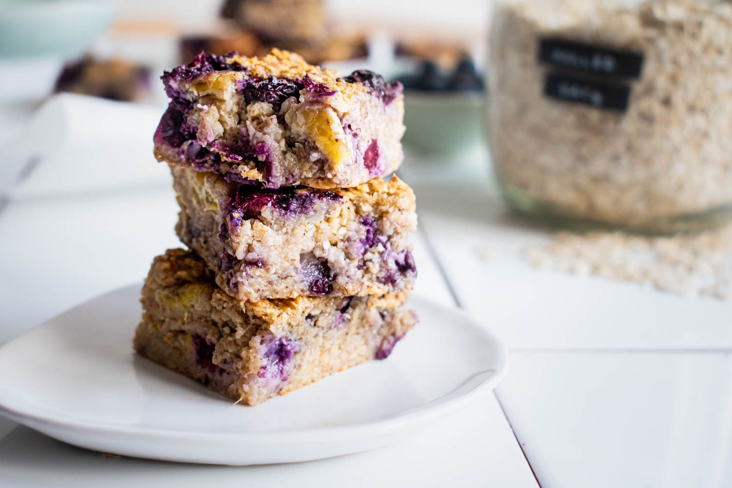 Baked blueberry banana oatmeal with rolled oats, fresh blueberries, and banana stacked on a plate with oats on the side.