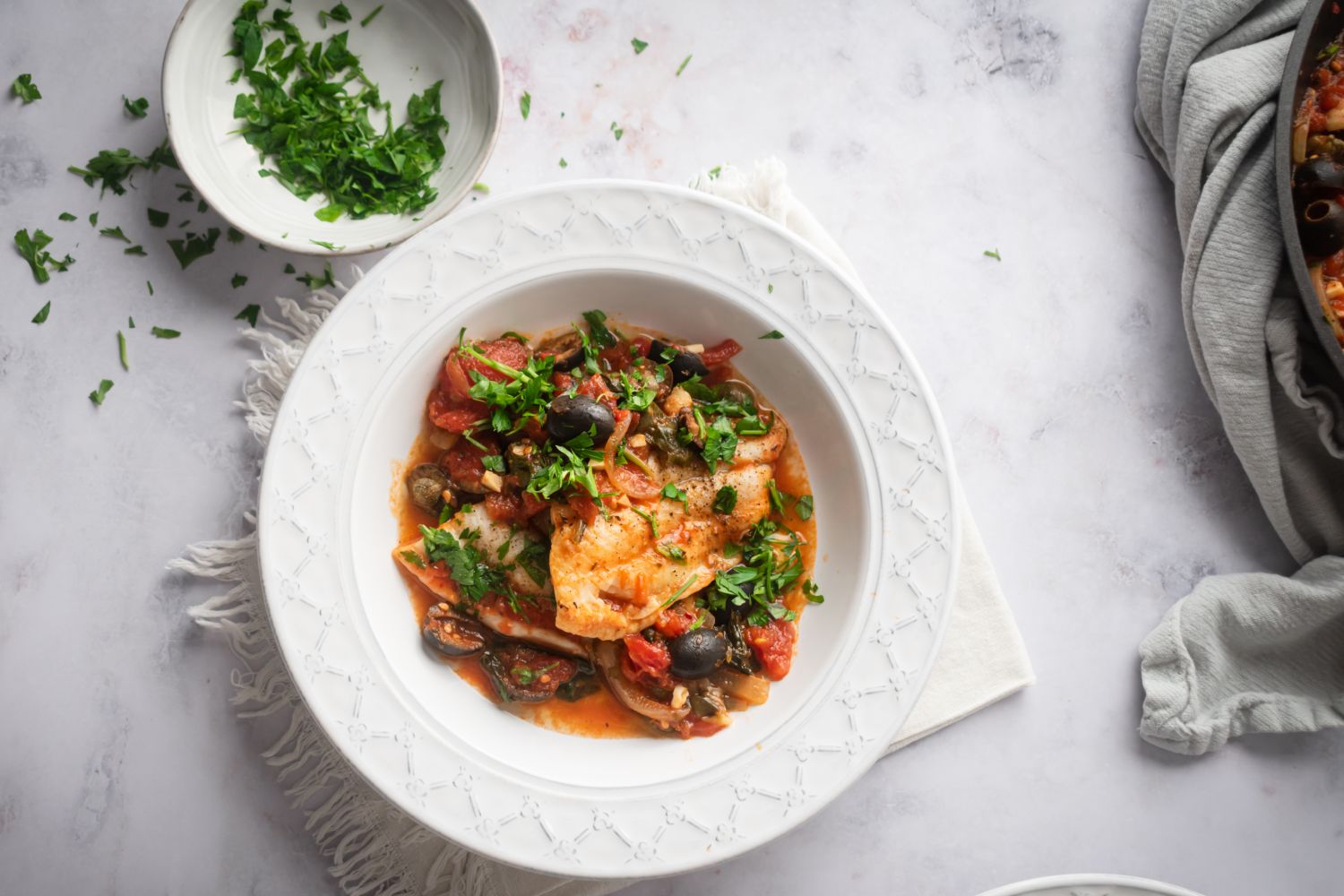 Baked Mediterranean fish cooked with tomatoes, black olives, spinach, onion, garlic, and capers in a bowl.