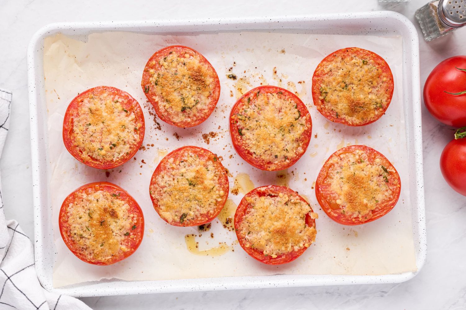 Baked parmesan tomatoes with lightly browned Parmesan cheese and herbs on a white baking sheet.