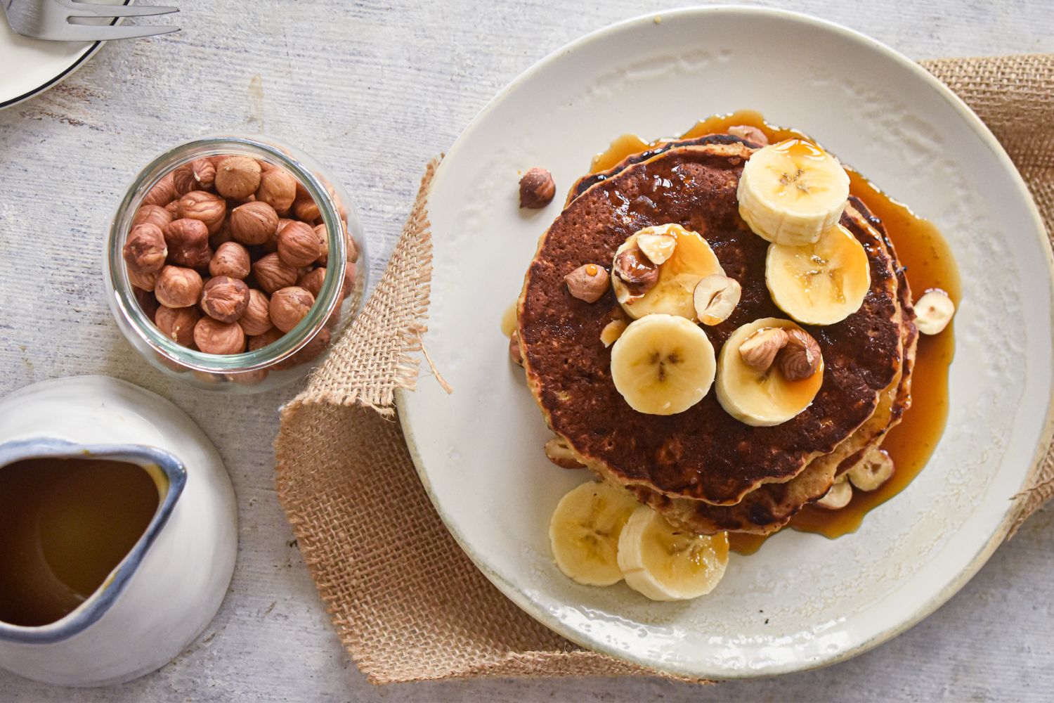 Banana oat pancakes made with mashed bananas and rolled oats stacked on a plate with maple syrup. 