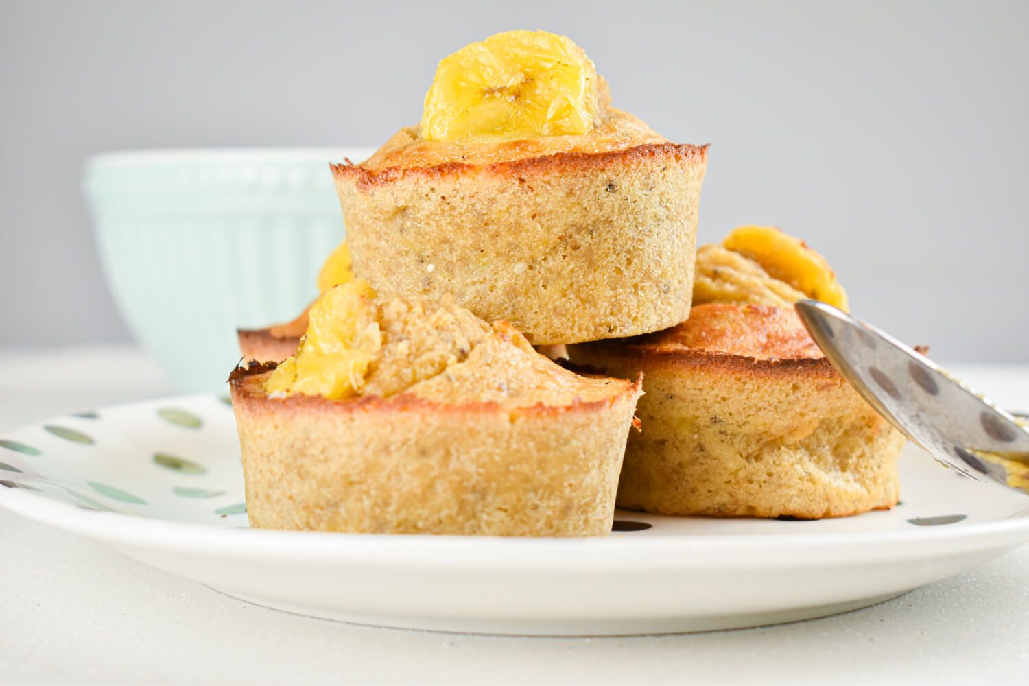 Banana muffins with quinoa and chia seeds with a sliced banana on top stacked on a plate.