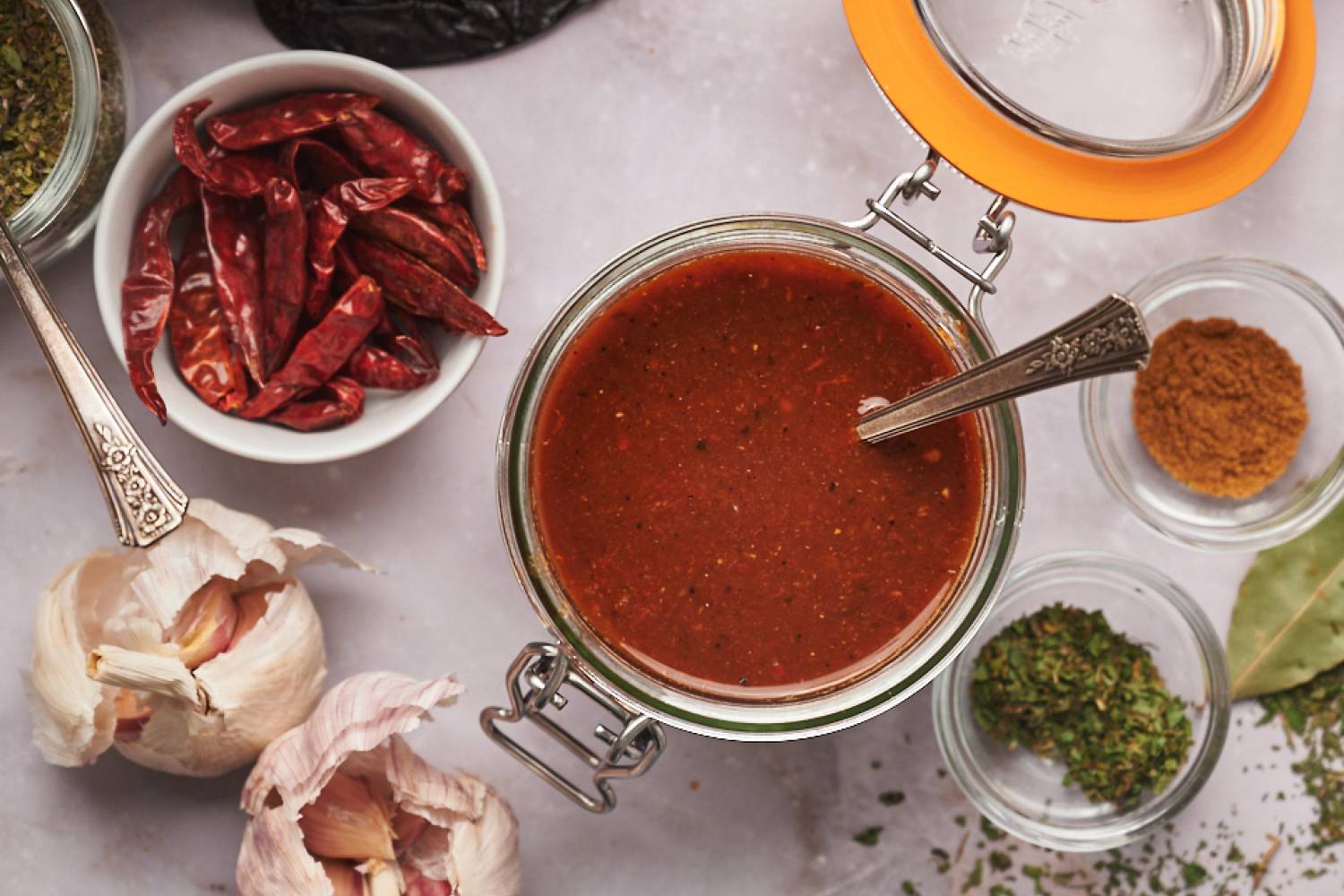 Birria sauce with dried chile peppers, garlic, onion, tomato, and spices in a glass jar.