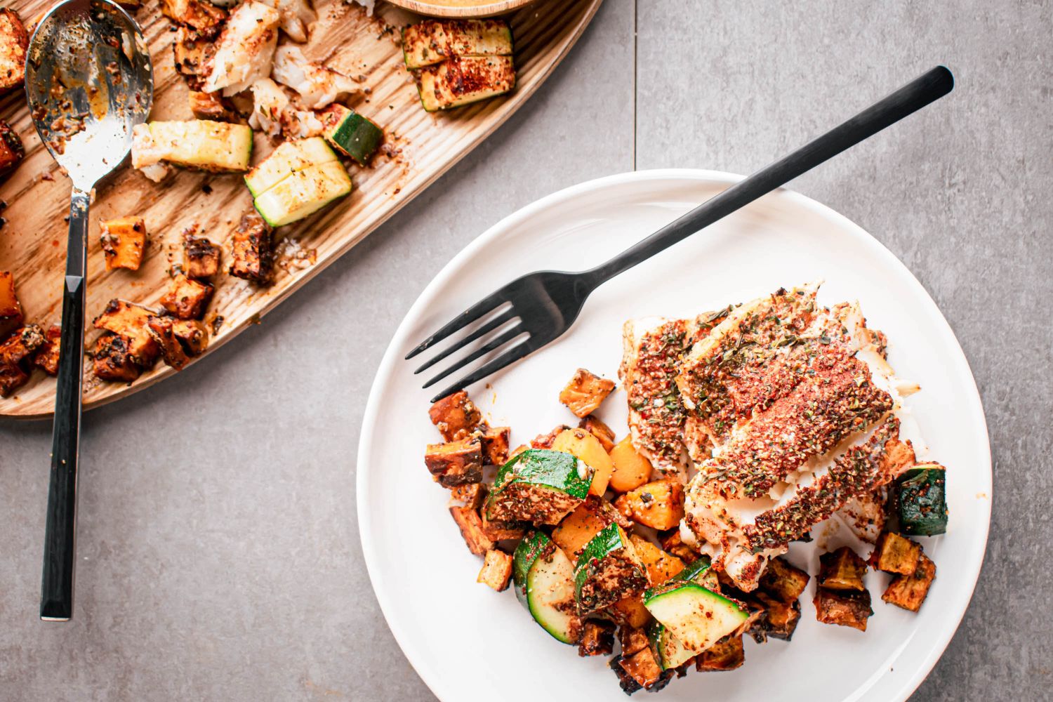 Blackened cod with vegetables cooked on a sheet pan and served on a plate with a fork.