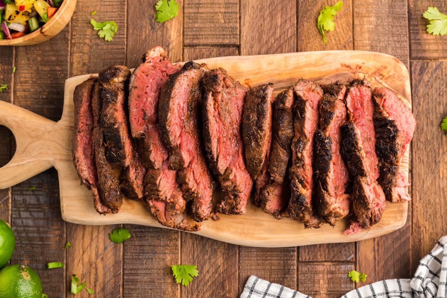 Blackened steak with a charred outside sliced on a wooden cutting board.