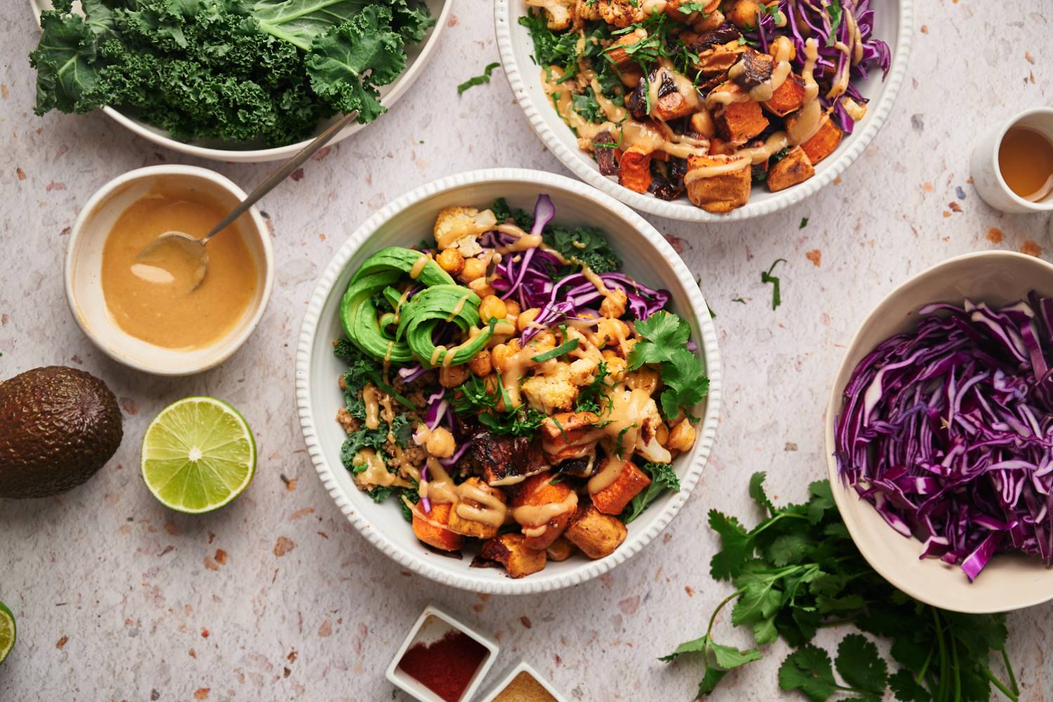 Buddha bowl with kale, chickpea, sweet potatoes, onions, and avocado served with maple tahini dressing.