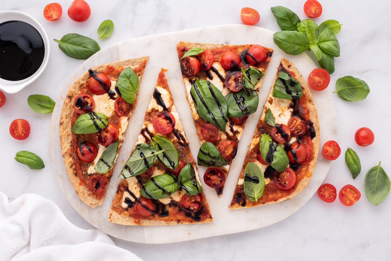 Caprese flatbead with cherry tomatoes, fresh mozzarella, basil leaves, and balsamic vinegar cut into four slices.