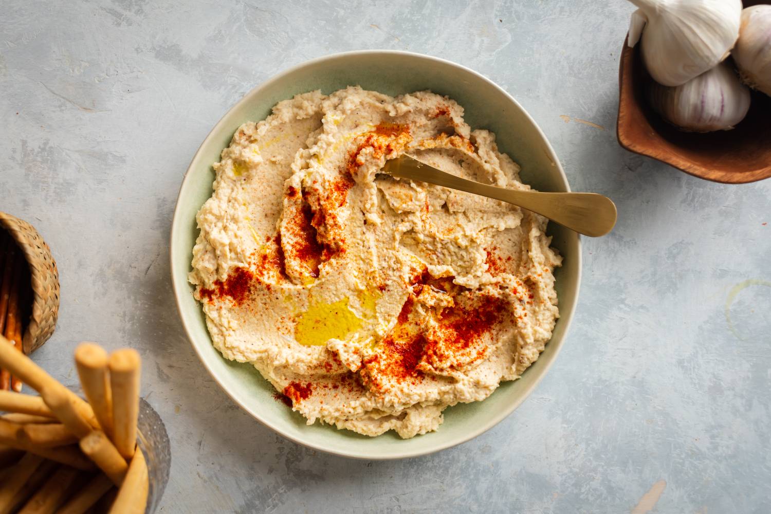 Cauliflower hummus with roasted cauliflower, tahini, olive oil, and lemon served in a bowl with breadsticks on the side.