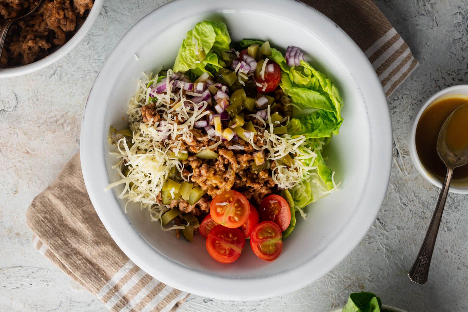 Cheeseburger salad with ground beef, pickles, tomatoes, lettuce, and shredded cheddar cheese in a bowl.