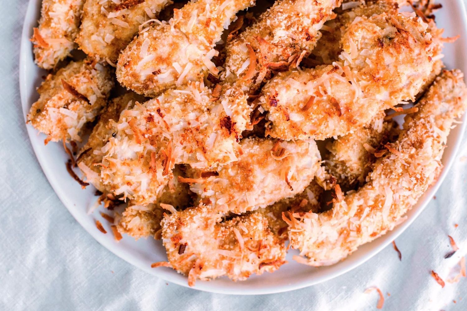 Coconut chicken fingers with a shredded coconut and spice breading on a white plate.