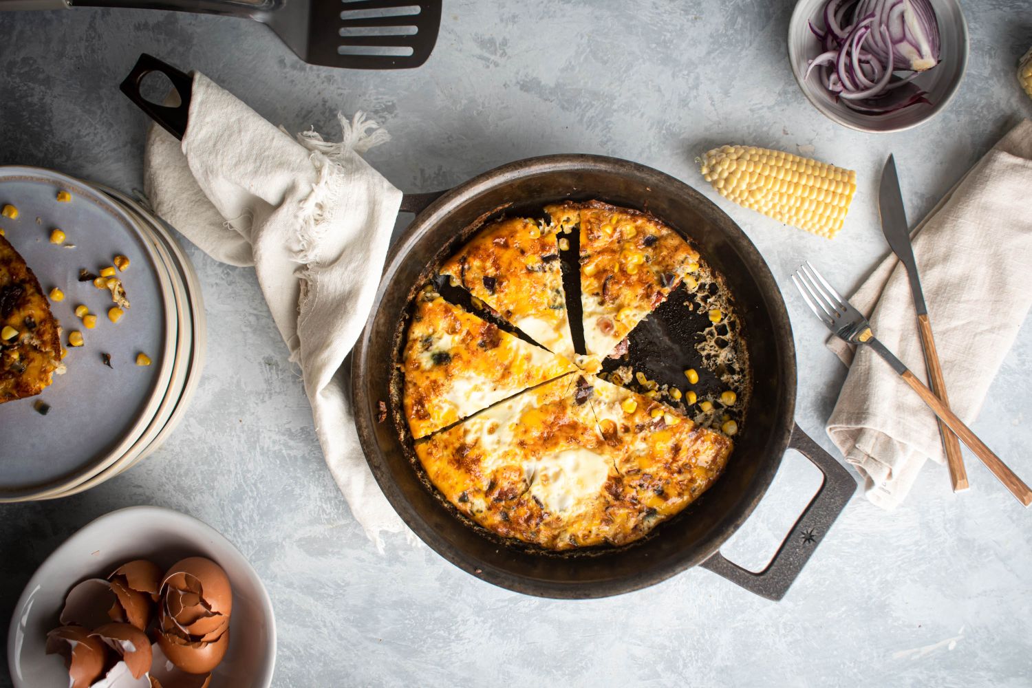 Corn and bacon frittata cooked with eggs, bacon, red onion, corn, and jalapeno in a skillet and sliced. 