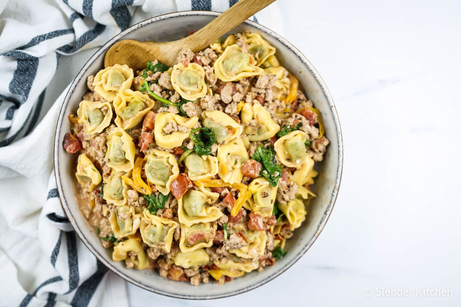 Creamy chicken tortellini in a creamy tomato sauce with fresh spinach in a bowl with a wooden spoon.