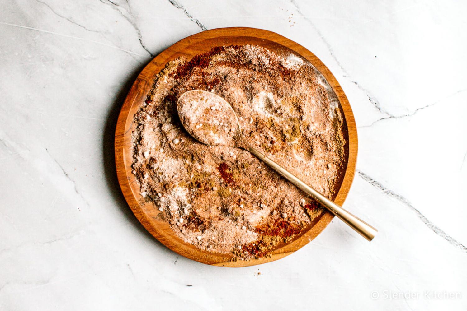 Fajita seasoning with chili powder, paprika, garlic powder, onion powder, and cumin mixed on a wooden plate.