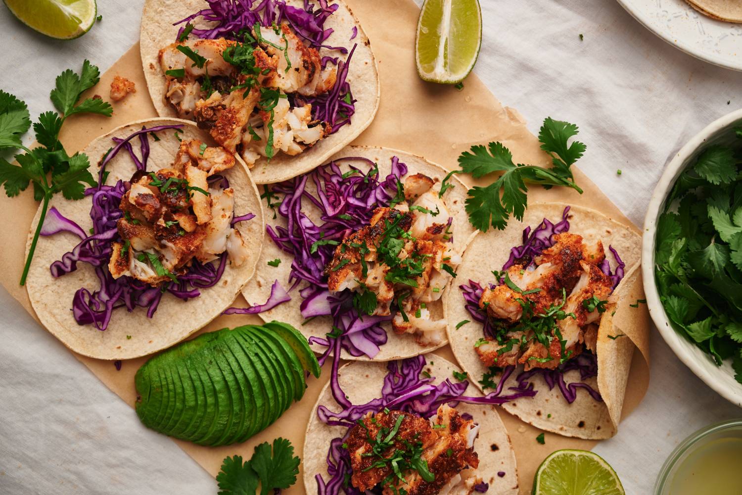 Fish tacos with flaky seasoned fish served in a corn tortilla with cilantro, shredded red cabbage, and limes. 