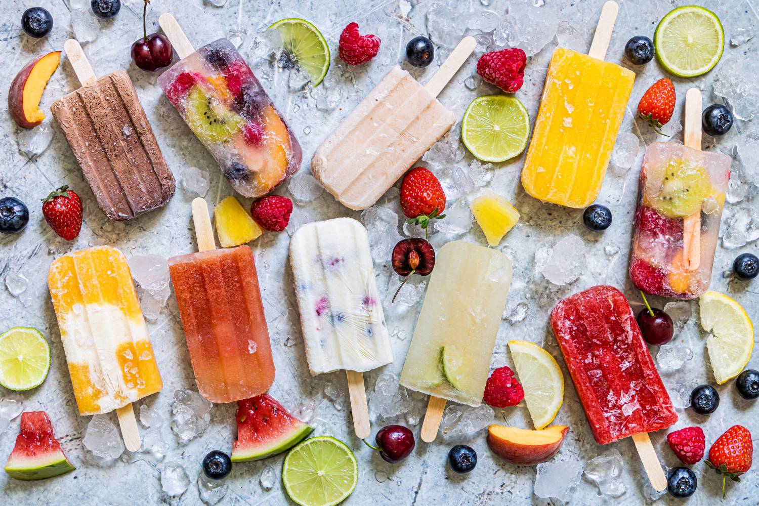 Fruit popsicles on a marble board with ice and fresh fruit. 