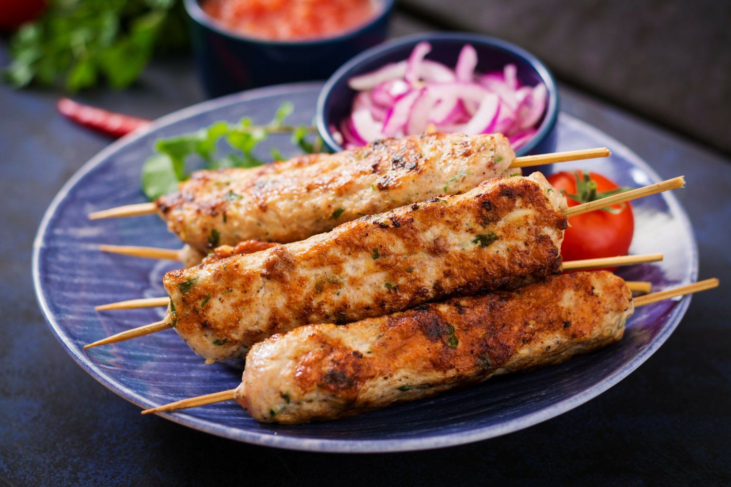 Grilled turkey lula kabobs with red onions, parsley, and lemon on a slate board.