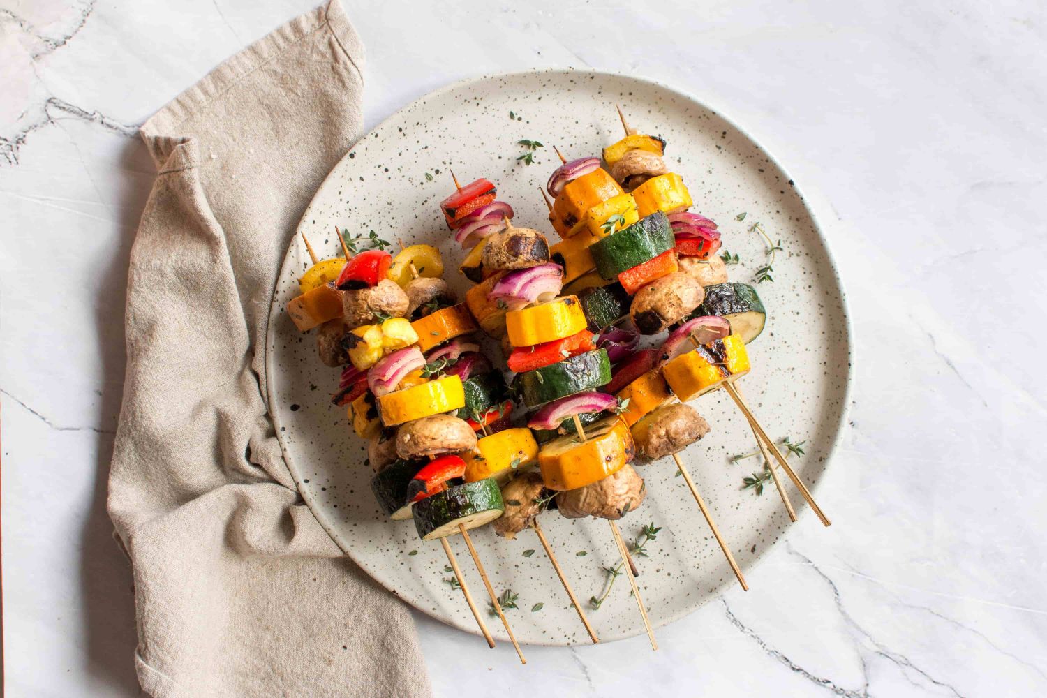 Grilled vegetable skewers with red onion, bell pepper, zucchini, summer squash, and mushrooms on wooden skewers.