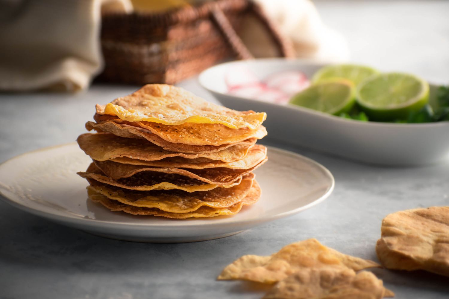 Homemade tostada shells with baked corn tortillas on a plate with limes, radishes, and cilantro on the side.