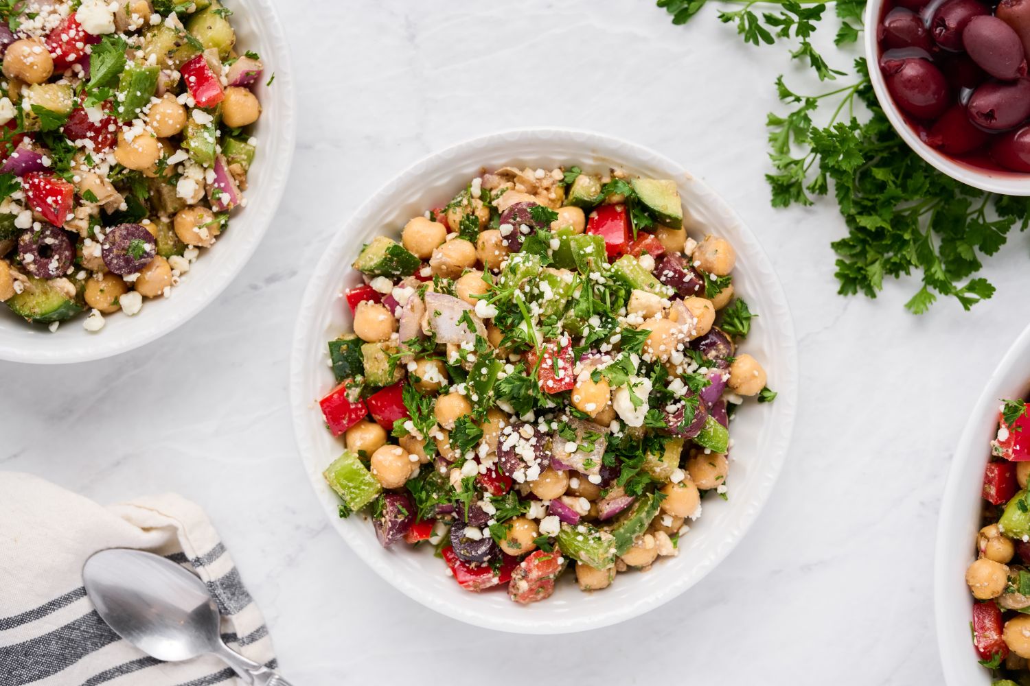 Mediterranean salad with chickpeas, olives, bell peppers, fresh herbs, and feta cheese in a bowl.