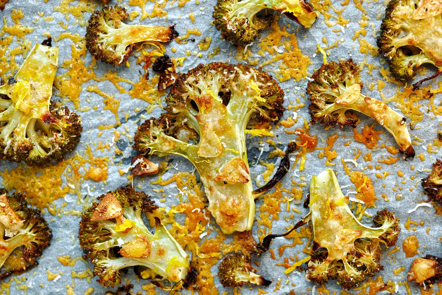 Parmesan roasted broccoli on a baking sheet with slices of garlic and melted cheese.