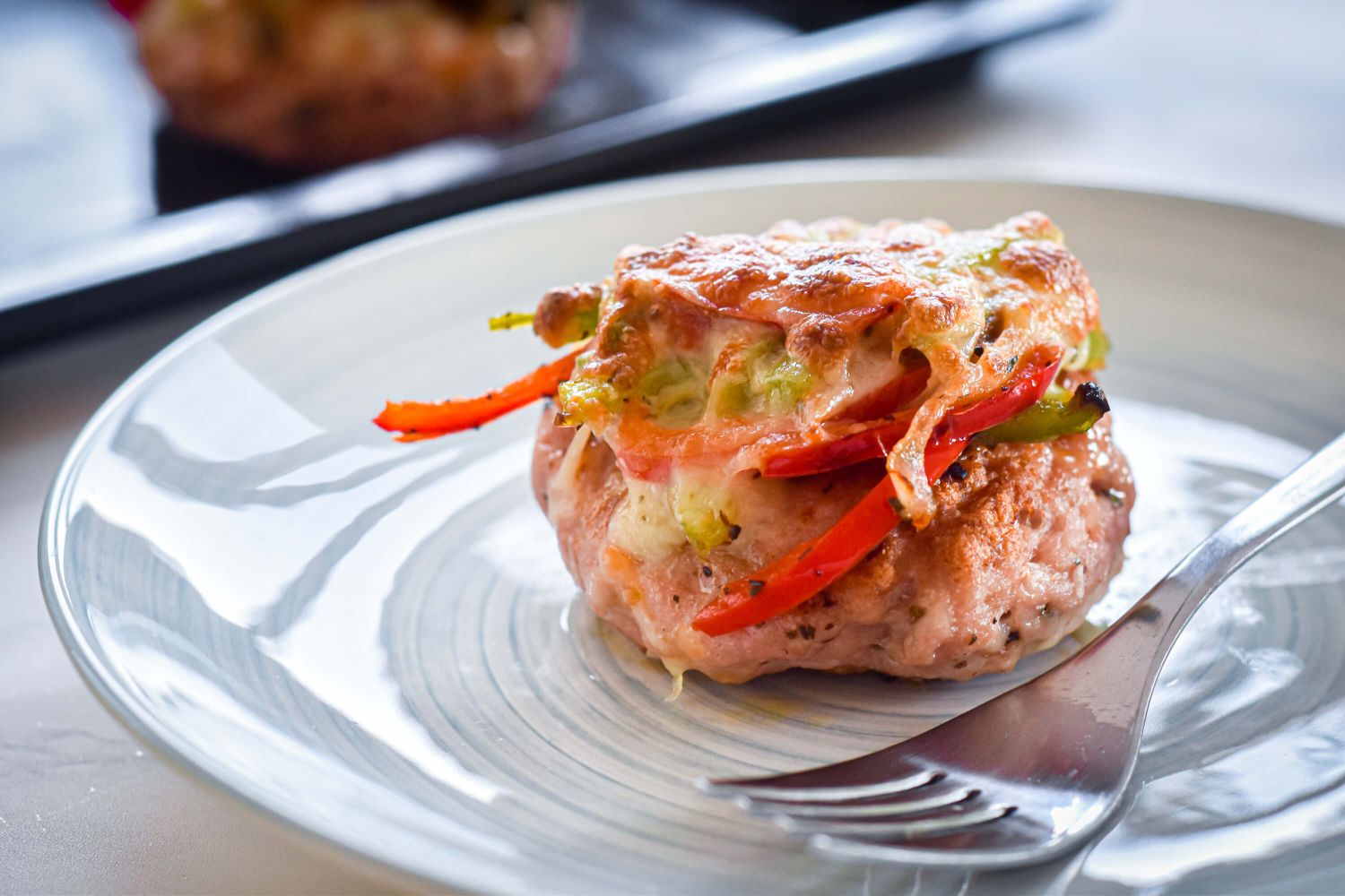 Pizza turkey burgers with marinara sauce, melted cheese, peppers, onions, and basil on a plate with a fork.