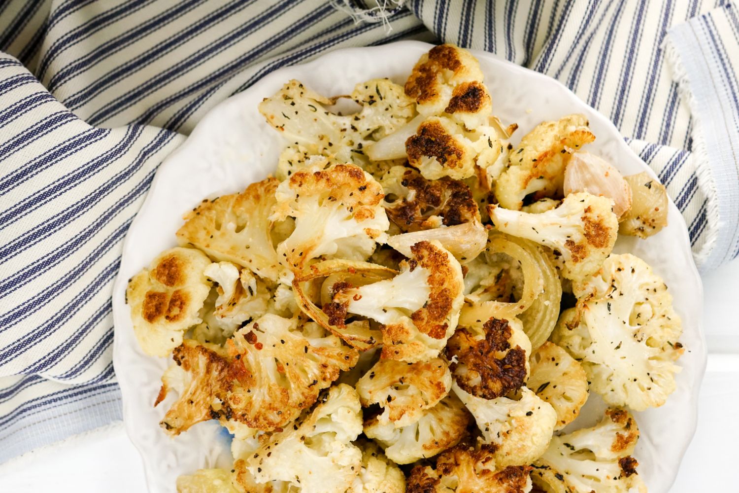 Parmesan Roasted Cauliflower with garlic cloves, parsley, and Parmesan cheese on a white plate.