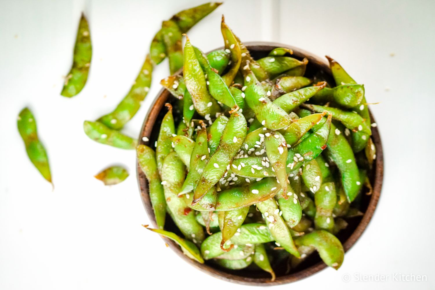 Stir fried edamame in a wooden bowl served with soy sauce and sesame seeds.