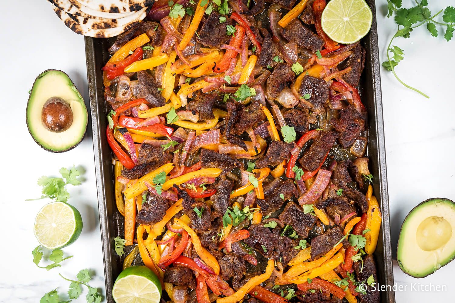 Sheet pan steak fajitas made with homemade fajita seasoning, flank steak, bell peppers, and onions on a sheet pan. 