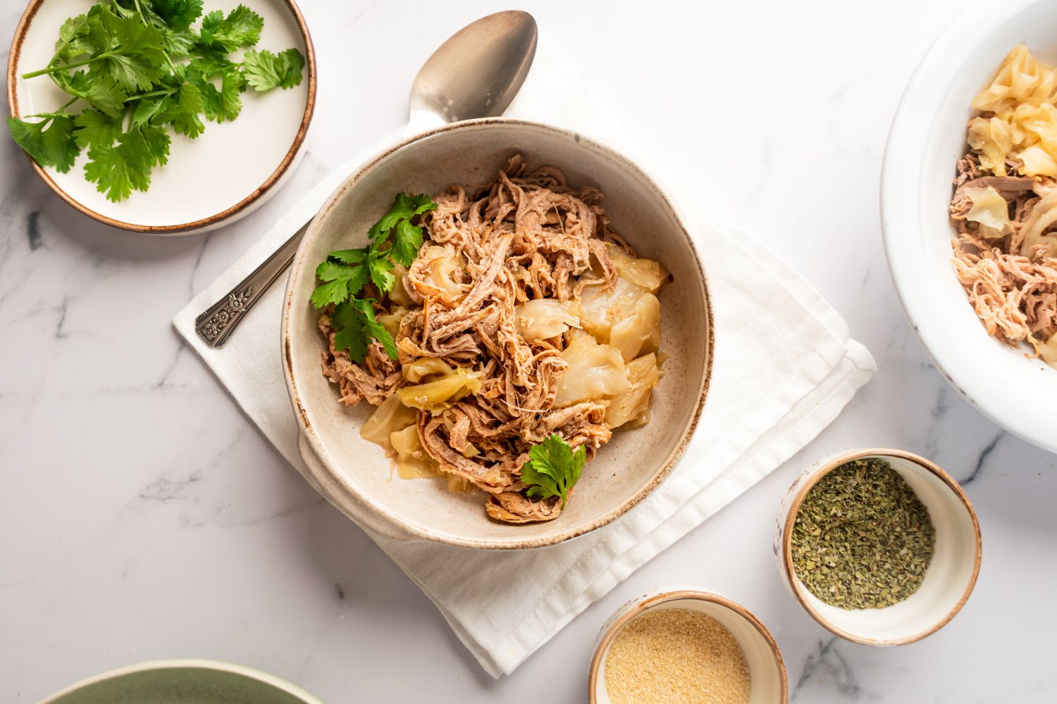 Slow cooker kalua pork with cabbage cooked with Hawaiian sea salt and liquid smoke in a bowl with cilantro on the side.