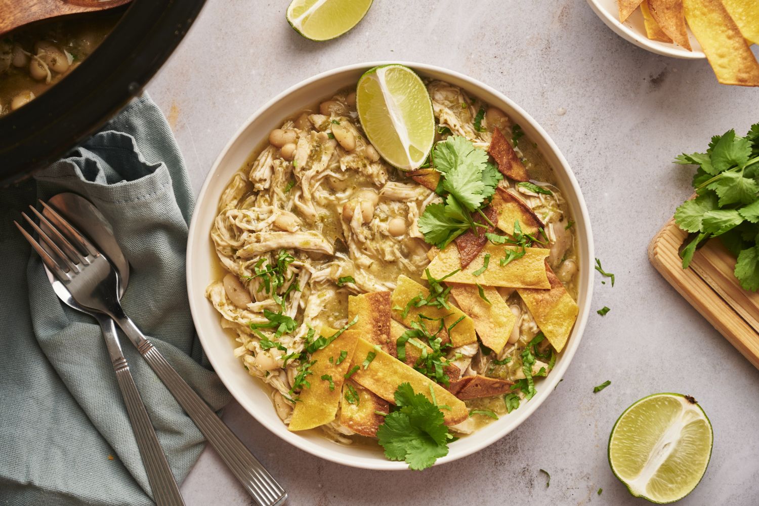 Slow cooker white chicken chili with shredded chicken, green chilies, white beans, tortilla chips, cilantro, and lime.