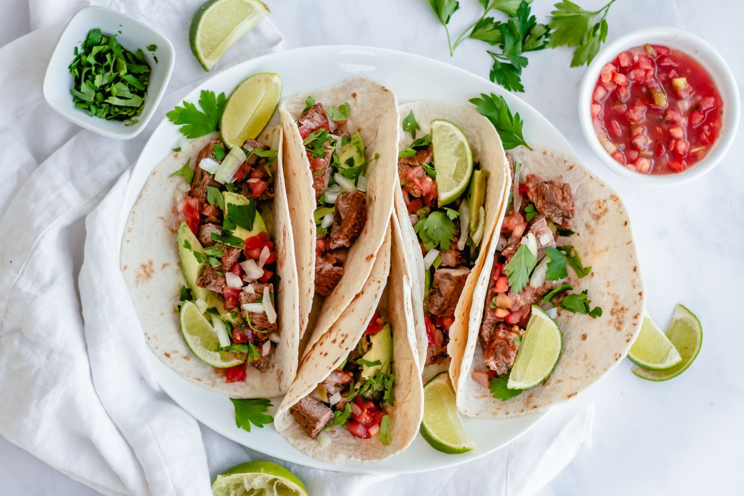 Steak tacos on flour tortillas with cilantro, onion, salsa, and lime.