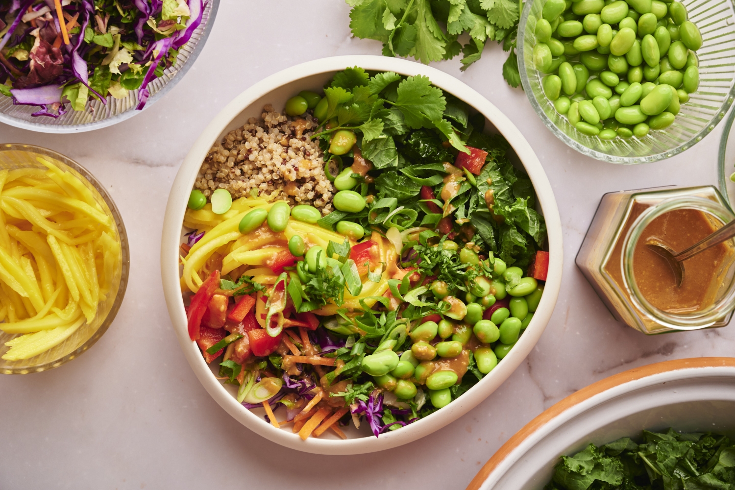 Thai bowls with quinoa, edamame, red bell pepper, kale, cilantro, and cabbage topped with peanut sauce.