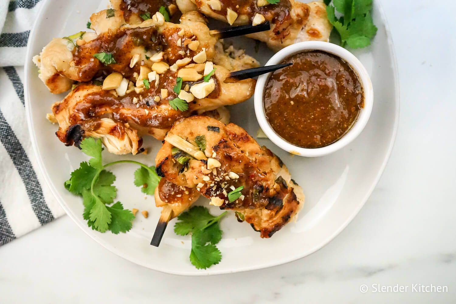 Thai peanut chicken skewers with green onions and peanut sauce on a plate.