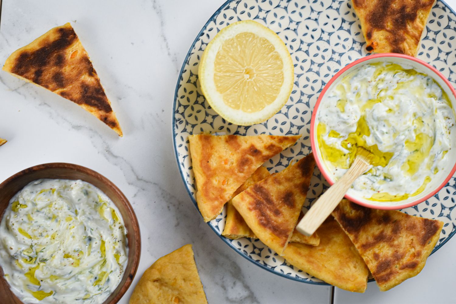 Tzatziki made with Greek yogurt, cucumbers, lemon, garlic, and dill in a bowl with pita wedges on the side.