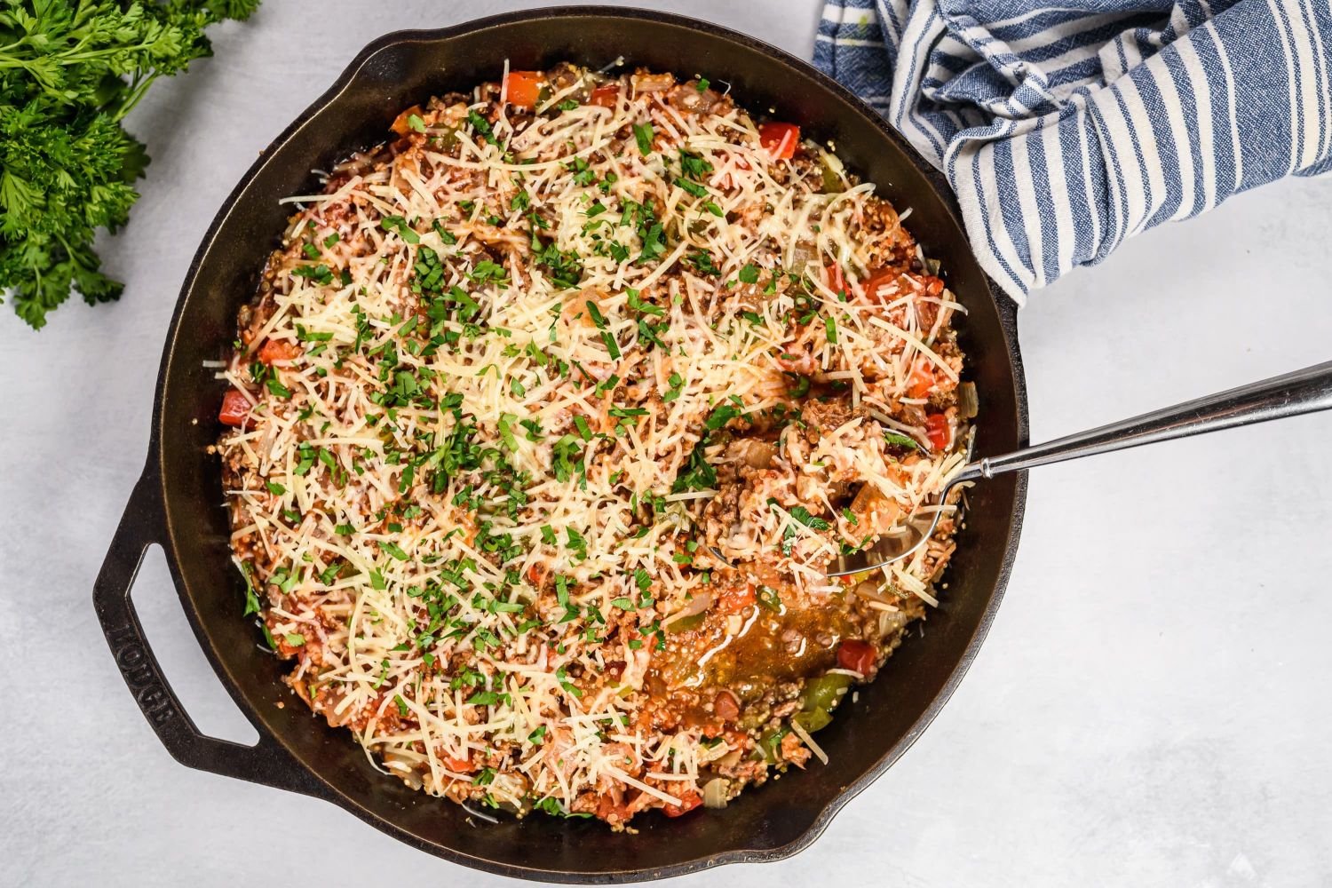 Unstuffed pepper skillet with ground beef, turkey sausage, quinoa, and bel peppers in a cast iron skillet topped with Parmesan cheese.