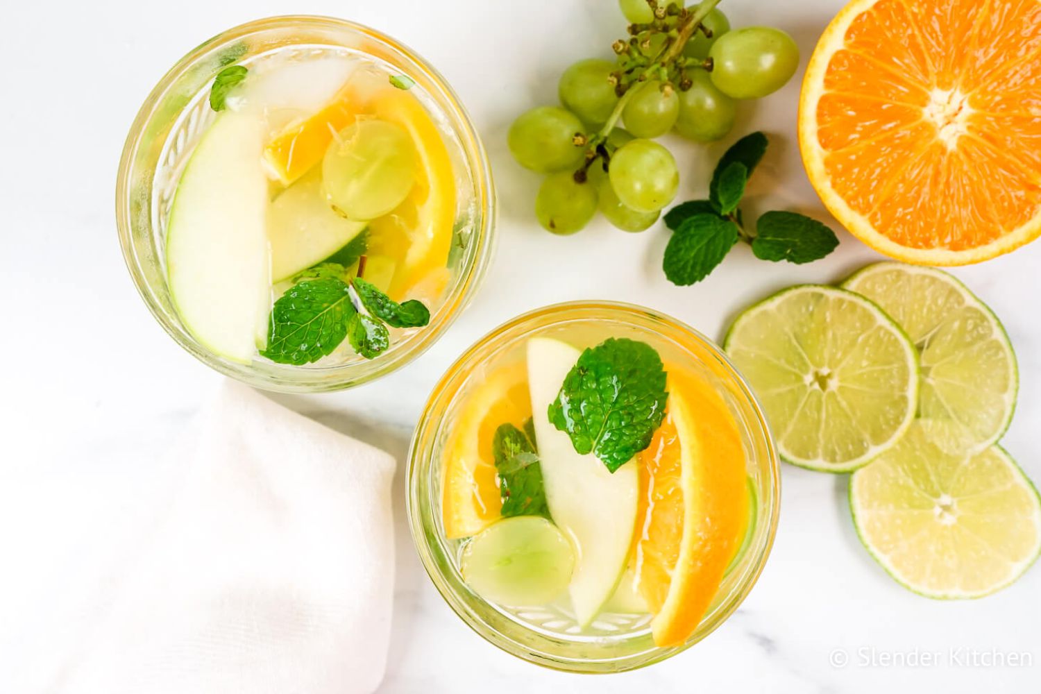 Vinho Verde white sangria with grapes, green apples, and orange in two glasses with fruit on the side.