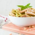 Pesto zoodles with chicken in a bowl with pine nuts on the side.