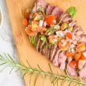 Spanish steak with tomato salad on a cutting board with rosemary.