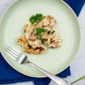 Greek chicken thighs with fresh parsley on a plate with a blue napkin.