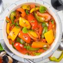 Pepperonata with bell peppers, sweet onion, Roma tomatoes, and garlic in a bowl with fresh basil and spices.