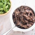 Sesame beef with thinly sliced flank steak in a sesame sauce in a bowl with sesame seeds.