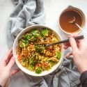 Asian quinoa stir fry with broccoli, carrots, cabbage, and snow peas in a bowl with stir fry sauce and sesame seeds.