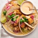 Baja fish tacos with crispy battered fish, cabbage slaw, pickled red onions, and white sauce served in corn tortillas on a plate.