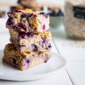 Baked blueberry banana oatmeal with rolled oats, fresh blueberries, and banana stacked on a plate with oats on the side.