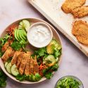 Baked chicken cutlets on a plate with salad and ranch dressing.