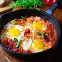 Baked eggs in tomato sauce with parmesan cheese on top in a cast iron skillet.