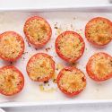 Baked parmesan tomatoes with lightly browned Parmesan cheese and herbs on a white baking sheet.