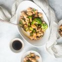 Basil chicken stir fry with broccoli florets, fresh lemon, soy sauce, and red pepper flakes in a bowl with a spoon.