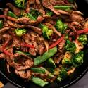 Beef stir fry with tender strips of beef with broccoli, carrots, bell peppers, and snow peas in soy stir fry sauce in a skillet.