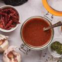 Birria sauce with dried chile peppers, garlic, onion, tomato, and spices in a glass jar.